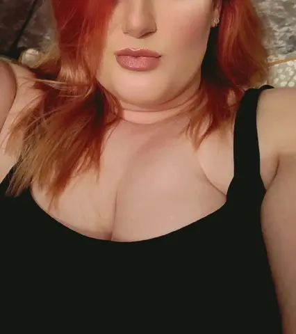 Redheaded woman in a black tank top relaxing indoors with a soft, natural mood.