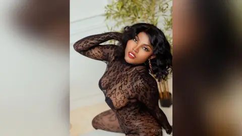 Elegant Black woman in a black lace bodysuit posing confidently against a soft indoor background.