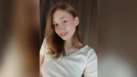 EvelinaMoorina smiling in a white lace top with her long blonde hair down.