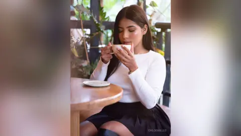 Young woman in a white long-sleeve top enjoying coffee at an outdoor cafe with a peaceful mood.