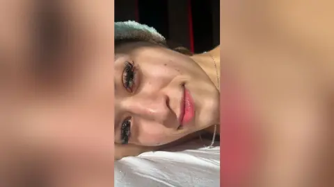 LuanaRodgers smiles at the camera while lying down with her head resting on a white pillow.