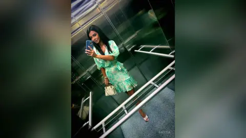 Young woman in a green floral dress taking a mirror selfie in a modern elevator.