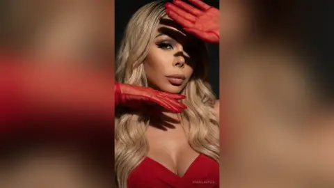 Glamorous blonde woman in a red dress and matching gloves posing with dramatic shadows in a studio setting.
