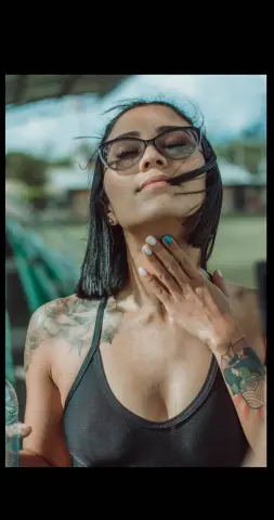 CelesteGrayy wearing glasses and a black tank top, posing outdoors with her hand on her neck.