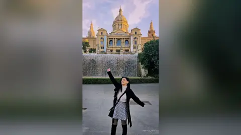 Cheerful woman in a black coat and plaid skirt raising her fist in front of the Sacré-Cœur Basilica in Paris.