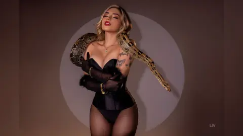 Glamorous woman in a black bodysuit with a large snake draped over her shoulders in dramatic studio lighting.