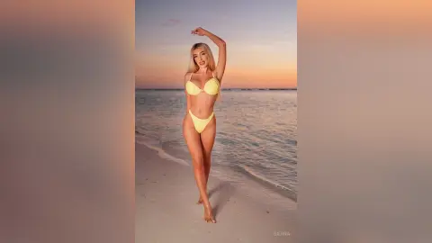 Blonde woman in a yellow bikini posing on a tropical beach at sunset.