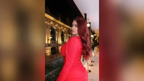 Elegant woman in a red evening dress posing at a luxury balcony at night.