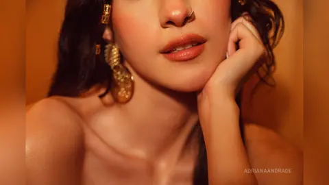 Close-up of a woman with glowing skin and large gold earrings posing in warm, golden lighting.