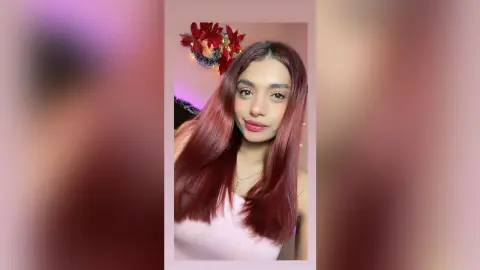 Young woman with long reddish hair wearing a white tank top in a festive room with holiday decor.