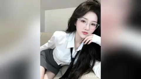 Young woman in white blouse and black tie sitting on a sofa with a thoughtful expression.