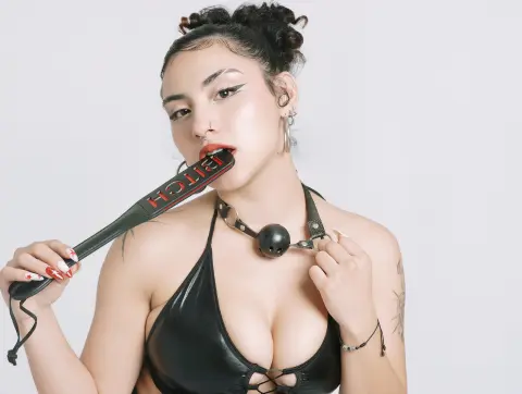 BrianaKnox — Young woman in a black leather bikini holding a black paddle with red text against a white background.