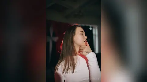 Young woman in a white long-sleeve shirt posing with a dreamy expression in moody red lighting.