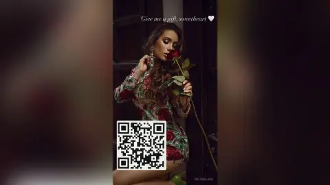 Elegant woman in a floral print dress holding a red rose in a moody, romantic indoor setting.