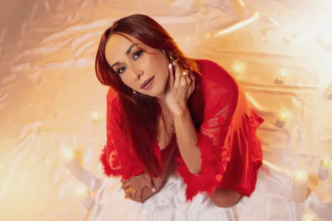 Elegant woman in a red silk robe relaxing amidst glowing candles on white fabric in warm lighting.