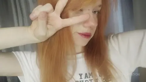 MozelleRozycki poses with a peace sign, showing her long red hair and a small nose piercing while wearing a white t-shirt.