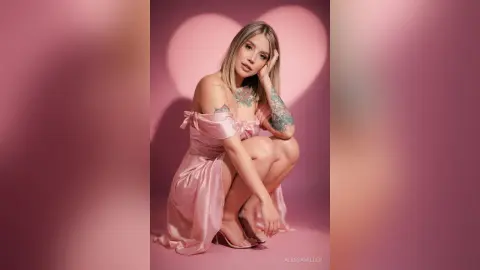 Blonde woman in a pink satin dress posing against a romantic heart-shaped shadow background.