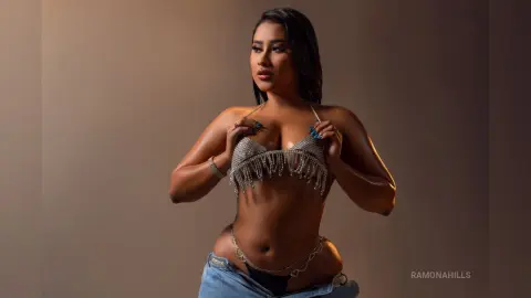 Confident woman in a silver sequin bikini top and denim jeans posing against a neutral studio background.