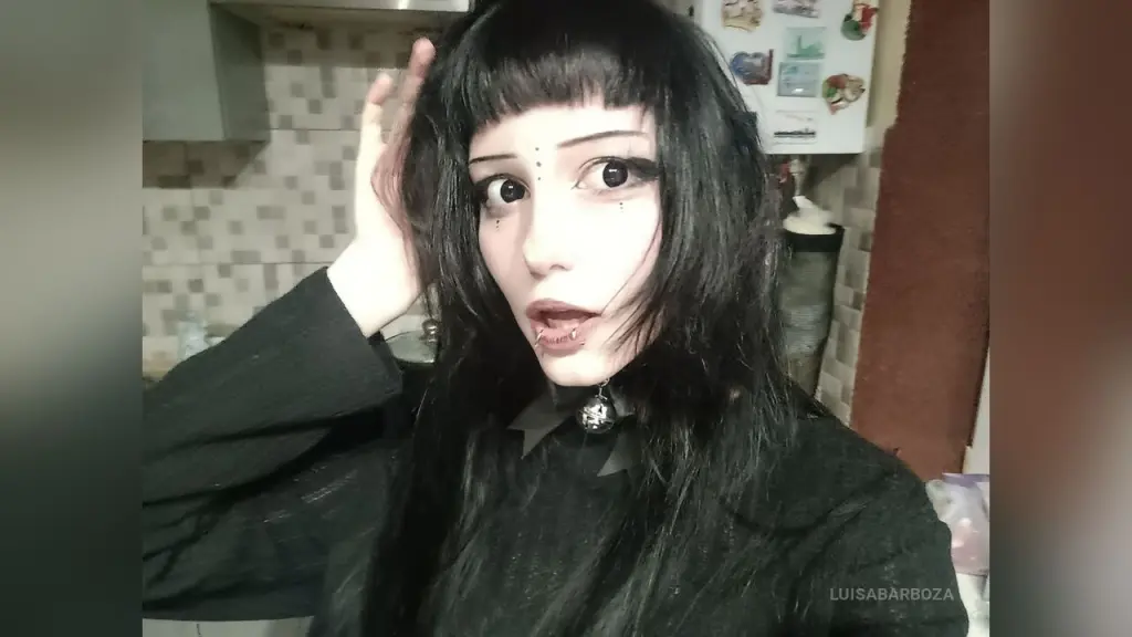 Goth woman with dark bangs and black outfit posing in a kitchen setting with a moody aesthetic.