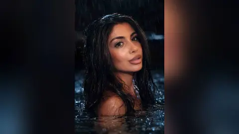 Beautiful woman with wet hair relaxing in a dark, moody outdoor pool during a night rain shower.