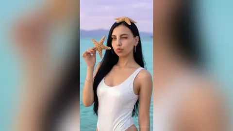 Playful woman in a white bodysuit holding a starfish on a sunny tropical beach background.
