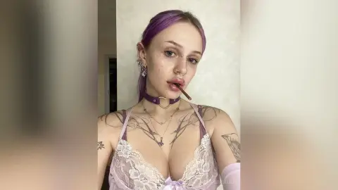 Young woman with purple hair in white lace lingerie and silver jewelry posing in a bright room.
