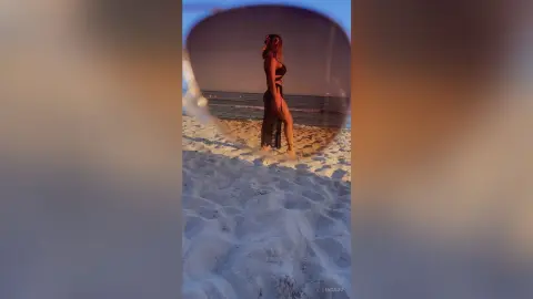 LindaDu stands naked on a sandy beach at sunset, showing her bare legs and body against the ocean waves.