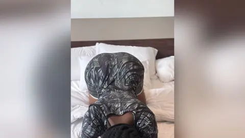 Woman in a grey patterned bodycon dress lounging on a white bed in a bright bedroom.
