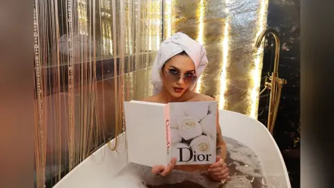 NerissaMist relaxes in a bubble bath with a white towel wrapped around her head, holding a Dior book in front of her chest.