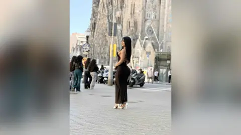 Elegant woman in a black evening gown posing in front of the Sagrada Familia in Barcelona.