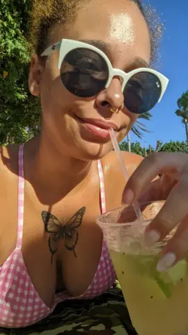 dominamoon — Smiling woman in white sunglasses and pink gingham bikini enjoying a refreshing summer drink outdoors.