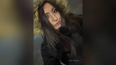 Young woman with long dark hair wearing a warm black winter parka with a faux fur hood in a moody setting.