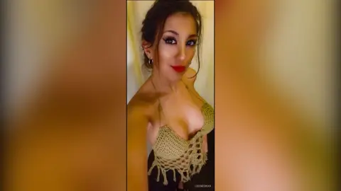 Glamorous woman in a beige crochet bikini top posing with bold red lipstick in a warm indoor setting.
