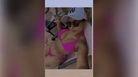Young woman in a pink bikini and white baseball cap relaxing outdoors in sunny summer weather.