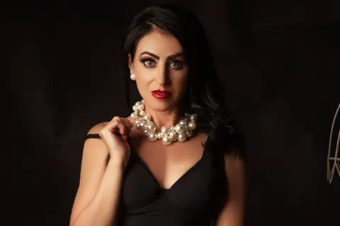 Elegant woman in a black dress and chunky pearl necklace posing against a dark background.