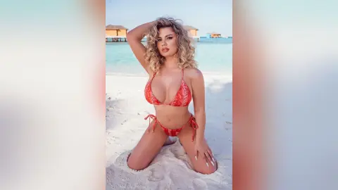 Blonde woman in a red bikini posing on a sunny tropical beach with turquoise water and villas.