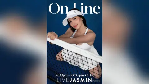 Smiling woman in white tennis outfit and visor leaning on a net against a blue background.