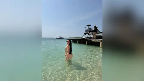 Young woman in a bikini wading in clear turquoise ocean water near a wooden pier on a sunny summer day.