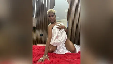 Young woman in a white satin wrap sitting on a red shag rug in a modern room with wood slat walls.