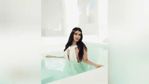 Ethereal woman in a white flowing dress and gold headpiece relaxing in a bright, minimalist luxury pool.
