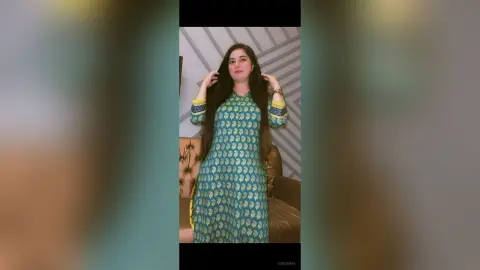 Young woman in a teal patterned ethnic tunic standing in a modern room with a serene expression.