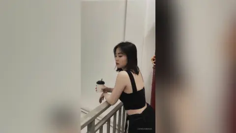 Young woman in a black crop top holding a coffee cup while leaning on a balcony railing in a minimalist setting.