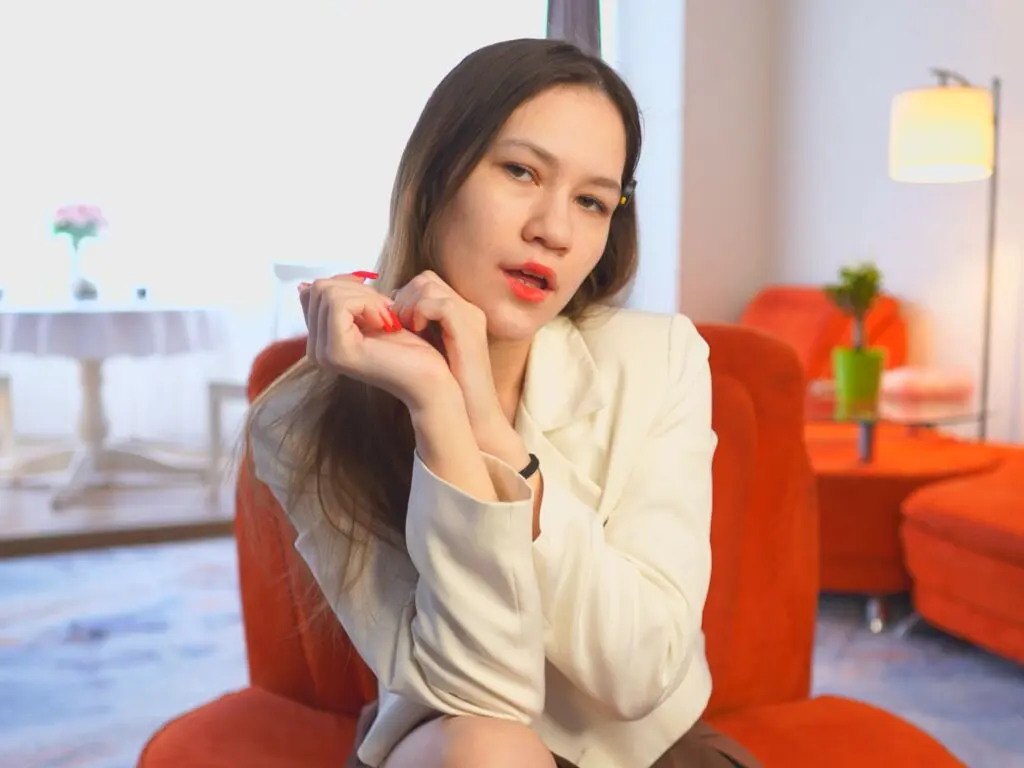 Young woman in a white blazer sitting on an orange armchair in a bright, modern living room.