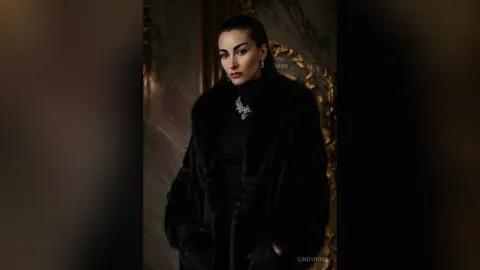Elegant woman in a luxurious black faux fur coat and necklace posing in a moody, vintage interior setting.