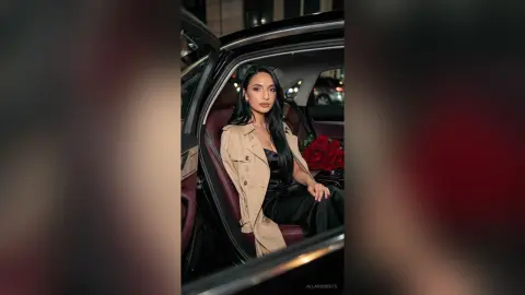 Elegant woman in a tan trench coat sitting in a luxury car with red roses, creating a sophisticated mood.