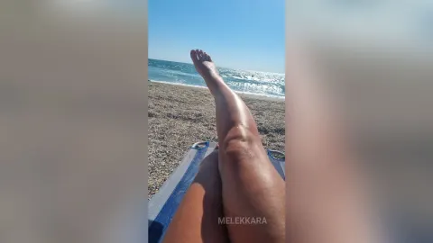 MelekKara — MelekKara relaxes on a blue beach towel with her legs stretched out toward the ocean waves.