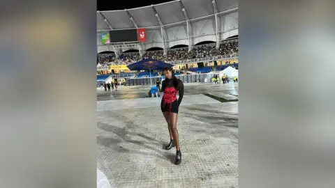 AmyJacobs stands in a large stadium wearing a red and black top with black shorts and black boots.