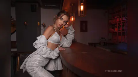 StacyHarland leans against a wooden bar wearing a silver glittery bra and matching trousers.