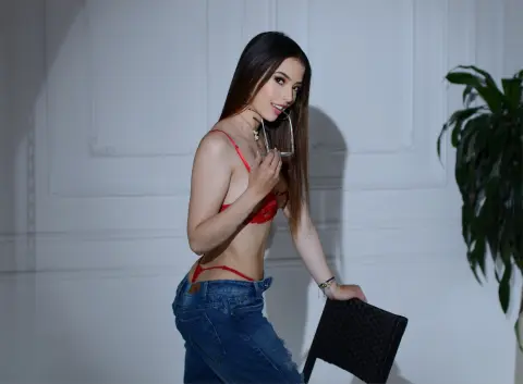 Young woman in red lace lingerie and blue jeans posing in a bright studio setting.