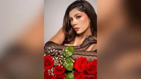 Glamorous woman in a black sheer outfit holding a bouquet of red roses in a moody studio setting.
